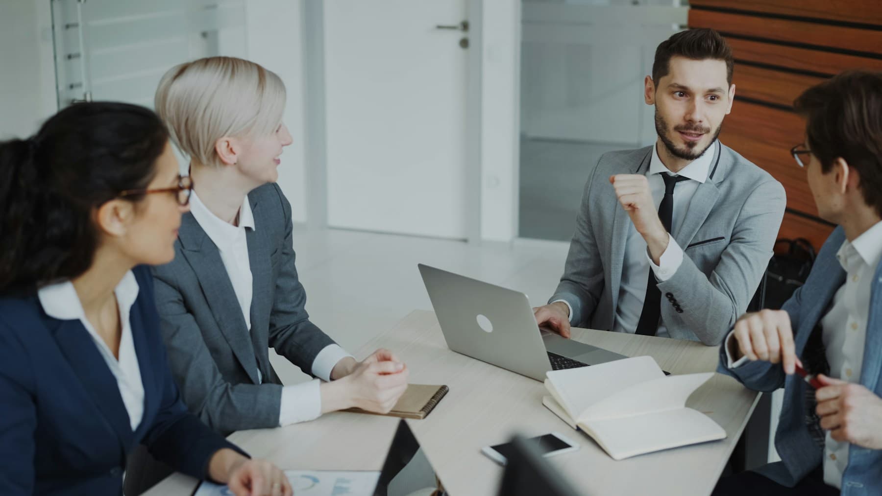 Four professionals in formal suits discussing ideas around a table